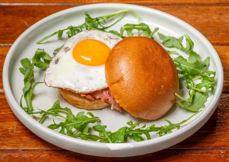 Classic bacon and egg roll on a brioche bun with a fried egg and Streaky Bacon, on a bed of rocket