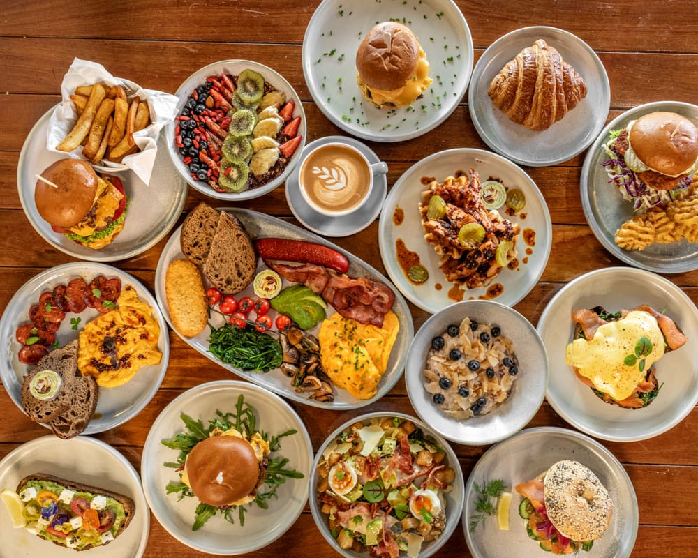A spread of Sunbrew Cafe breakfast and lunch dishes on a timber table, with a latte in the middle